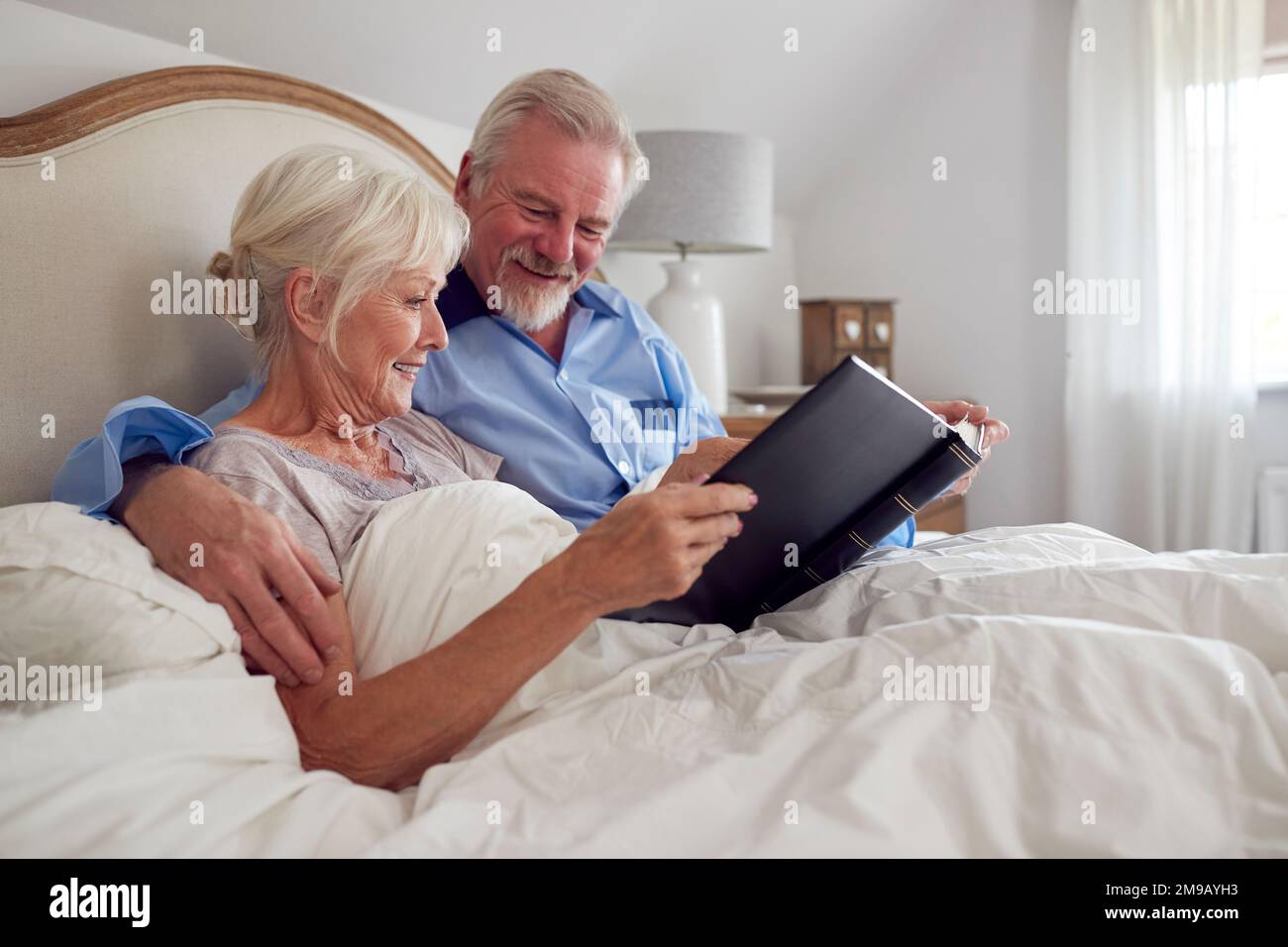 Seniorenpaar Im Bett Zu Hause, Das Sich Zusammen Ein Fotoalbum Anschaut Stockfoto