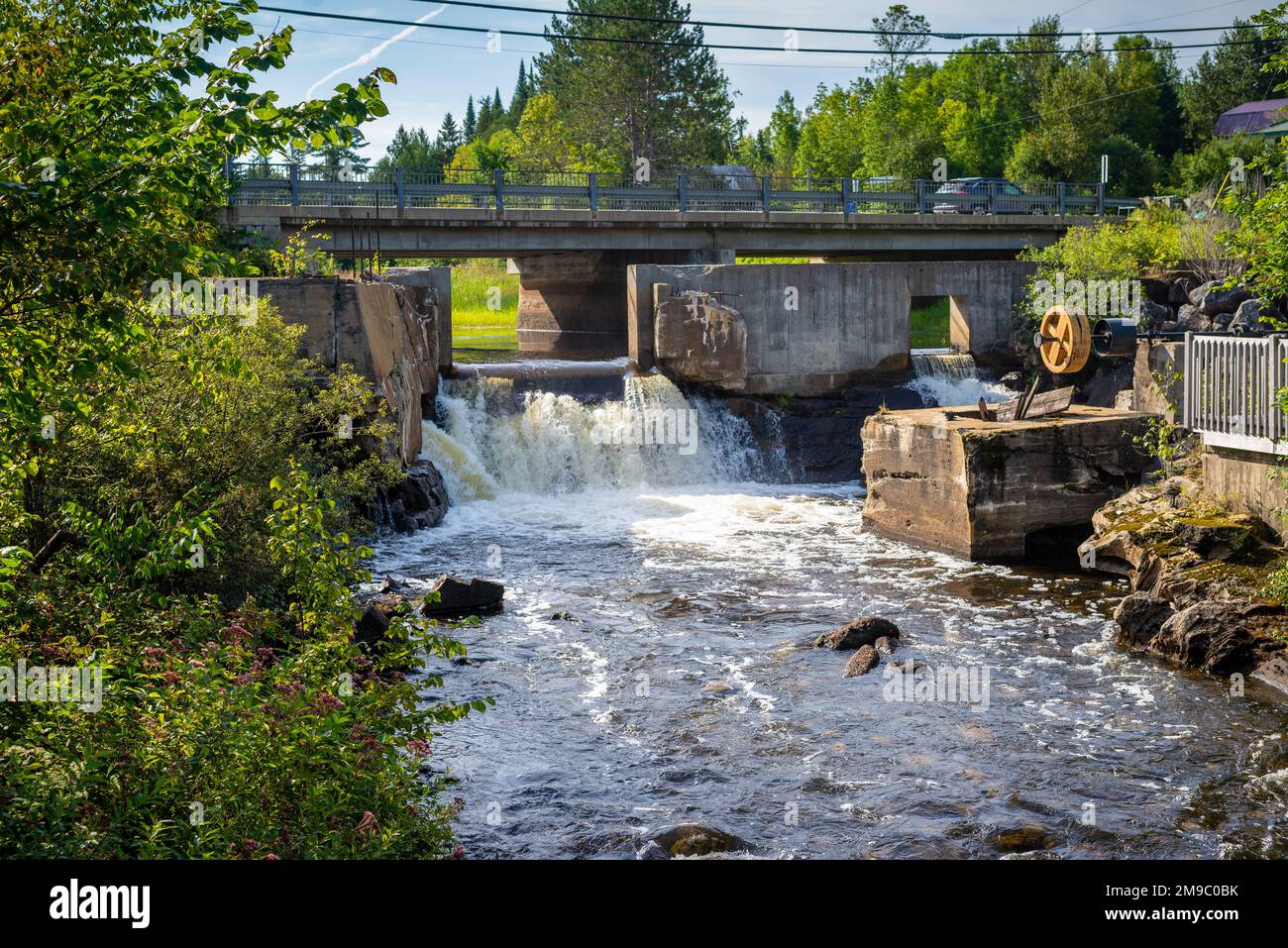 Eine Straßenbrücke über einen kleinen Fluss und einen gebrochenen Damm in den Laurentians, Quebec, Kanada. An einem sonnigen Sommernachmittag ohne Leute aufgenommen. Stockfoto