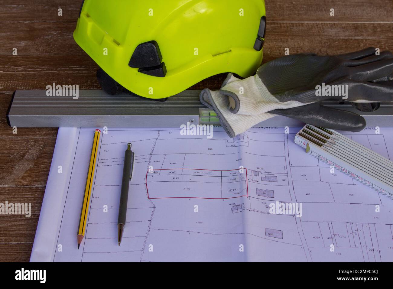 Abbildung eines Arbeitstisches mit Zeichnungen von Grundstücksplänen und Bauprojekten auf Elektro- und Arbeitshandschuhen. Stockfoto