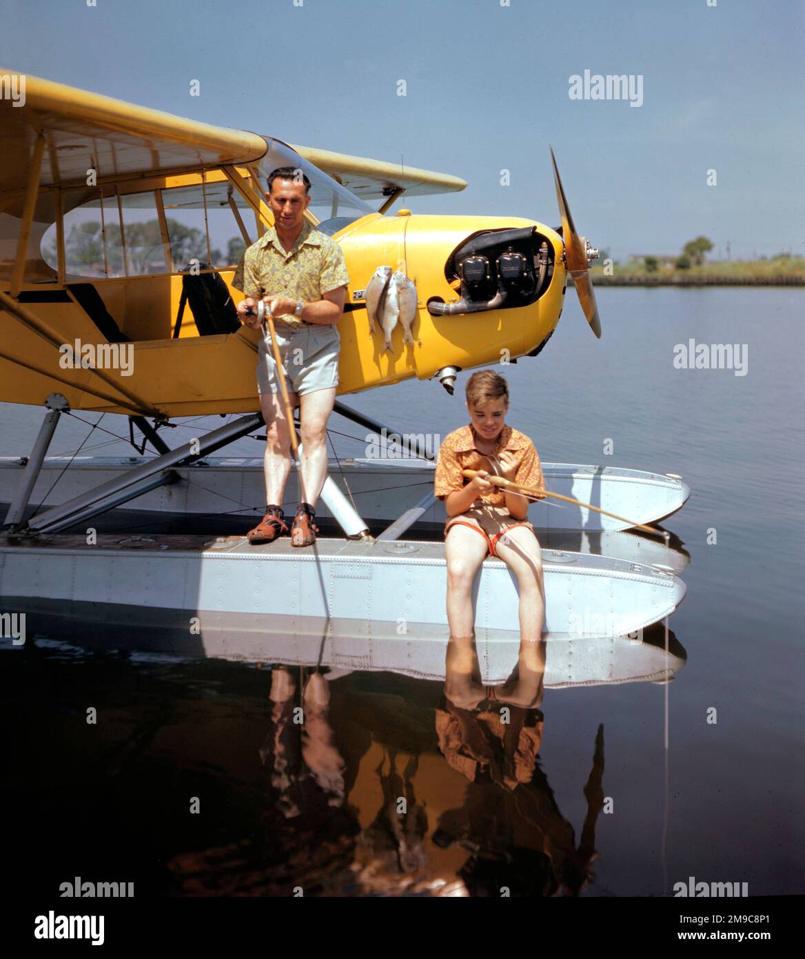 Piper J3-65 Cub Float-plane, mit Vater und Sohn, die von einem Floß fischen. Stockfoto
