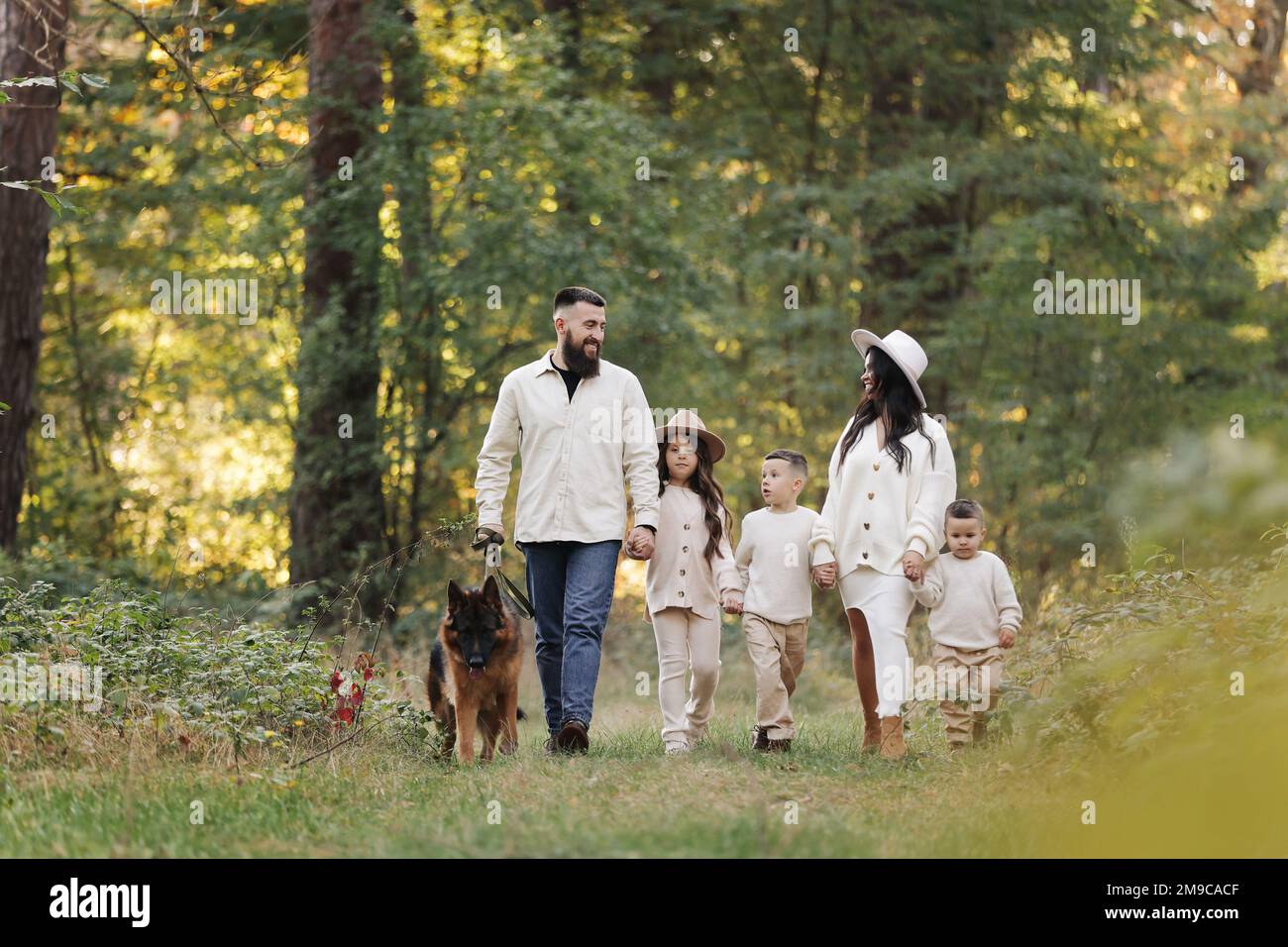 Fröhliche verspielte Familie, die mit Haustier im Park läuft. Junge mom, Dad, der Spaß mit drei Kindern und dem großen Hund draußen hat. Eltern mit Kindern, die Händchen halten. Akt Stockfoto