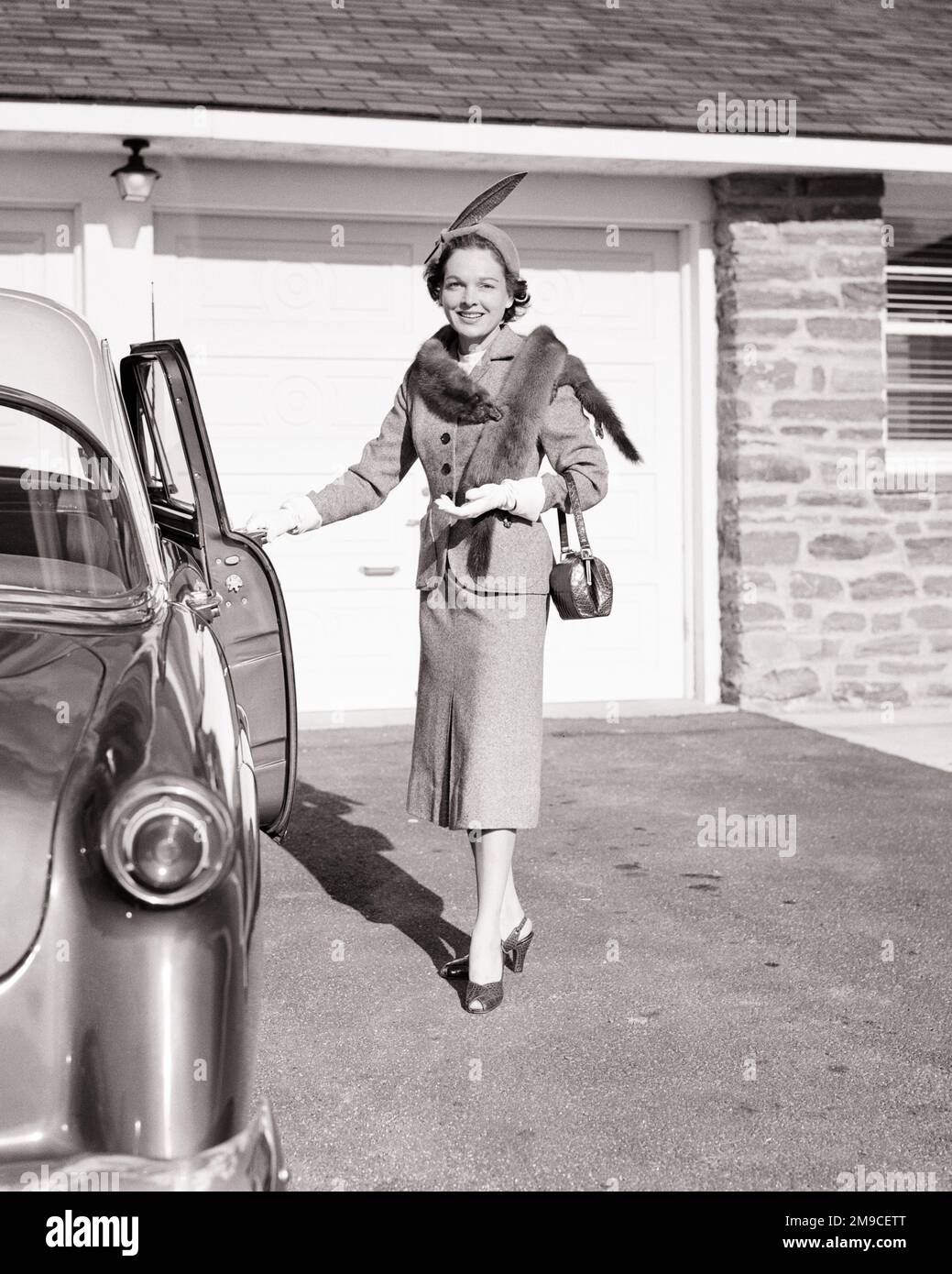 1950S MODISCH GEKLEIDETE FRAU IM ANZUG PELZMÜTZE MIT FEDERHANDSCHUHEN HOHE ABSÄTZE ÖFFNEN DIE AUTOTÜR LÄCHELND IN DIE KAMERA - M1607 HAR001 HARS MODISCH REICH ERFREUT FREUDE LEBENSSTIL ZUFRIEDENHEIT FRAUEN GESUNDHEIT ZUHAUSE KOPIERRAUM VOLLE LÄNGE DAMEN PERSONEN AUTO SELBSTVERTRAUEN TRANSPORT B&W BLICKKONTAKT GLÜCK FRÖHLICHE STYLES AUTOS EXTERIEUR STOLZ LÄCHELT GEHOBENE WOHLHABENDE AUTOS FRÖHLICHE, STILVOLLE FAHRZEUGE MODE PELZE MID-ADULT-MID-ADULT-FRAU MINK STAHL WOHLHABENDE SCHWARZ-WEISSE WEISSE WEISSE ETHNISCHE ZUGEHÖRIGKEIT HAR001 ALTMODISCH Stockfoto
