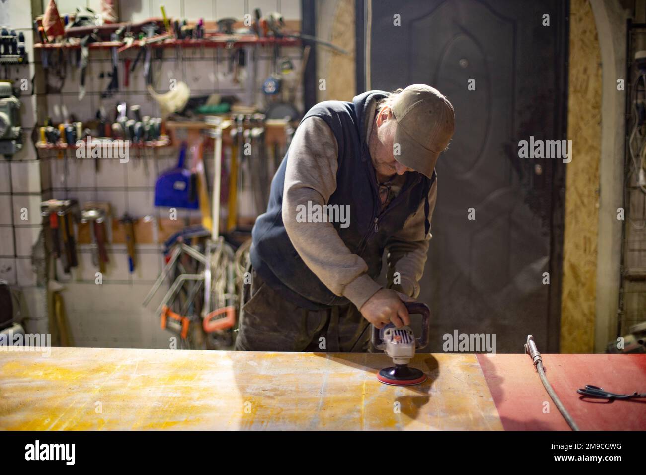 Mann schleift den Tisch. Der Typ in der Werkstatt arbeitet an Bord. Stockfoto
