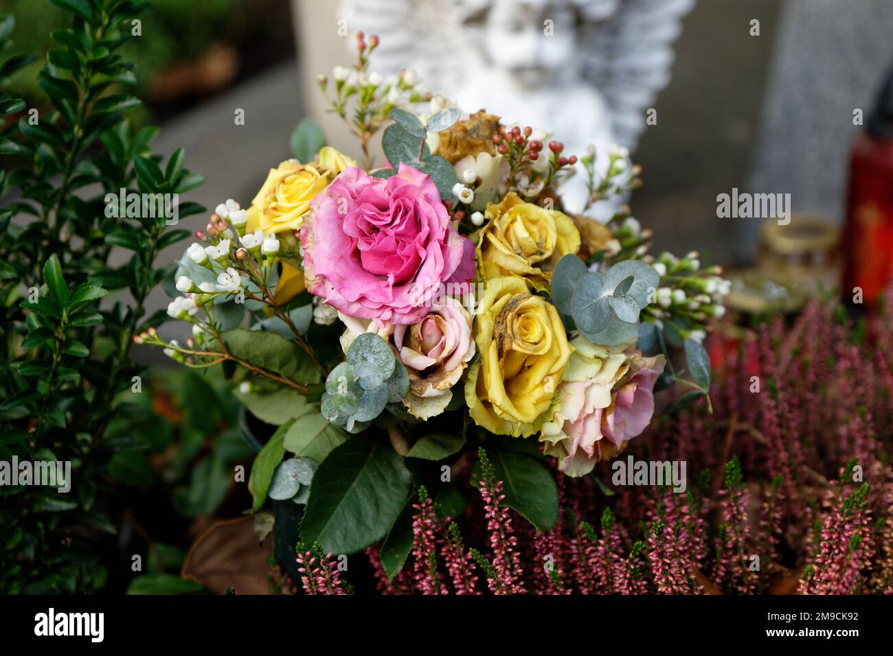 Verblasste Pastellrosen auf einem Grab vor einem Engel mit verschwommenem Hintergrund Stockfoto