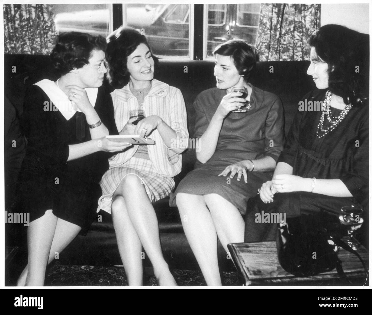 Vier junge Frauen geben eine Schachtel Pralinen und teilen sich ein zivilisiertes Glas Wein in einem Pub. Stockfoto