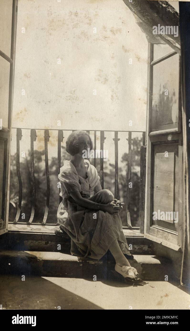 Ein Mädchen sitzt in einem offenen, durchgehenden Fenster Stockfoto