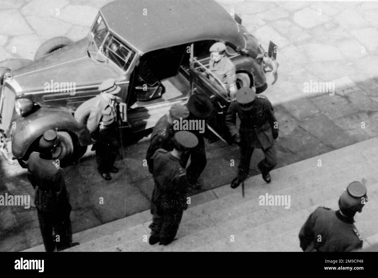 Eine Gruppe britischer Armeeoffiziere, die mit dem Auto an einem unbekannten Ort in Deutschland ankommen, fotografiert von einem oberen Stockwerk des Gebäudes, in das sie eintreten. Stockfoto