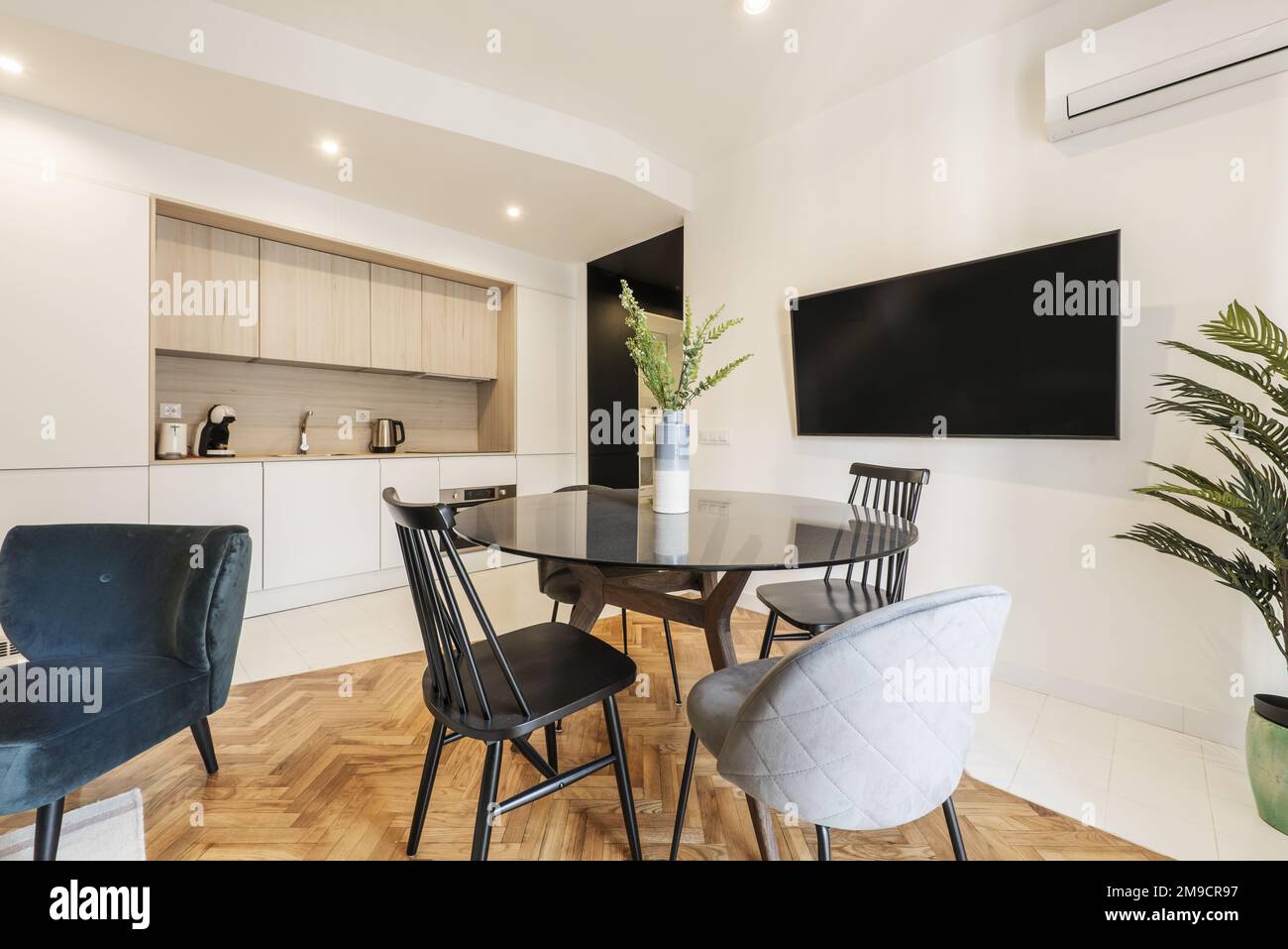 Loft mit rundem, schwarzem Glasesstisch mit Vase und offener Küche in modernem Design, Fernseher an der Wand und verschiedene Stühle mit lackiertem oa Stockfoto