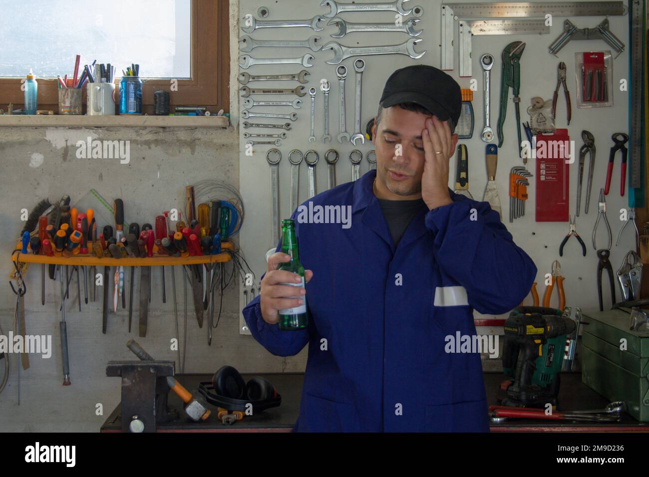 Bild eines Mannes im Overall mit einer Flasche Bier in seiner Werkstatt. Pause, entspannen Sie sich nach der Arbeit. Stockfoto