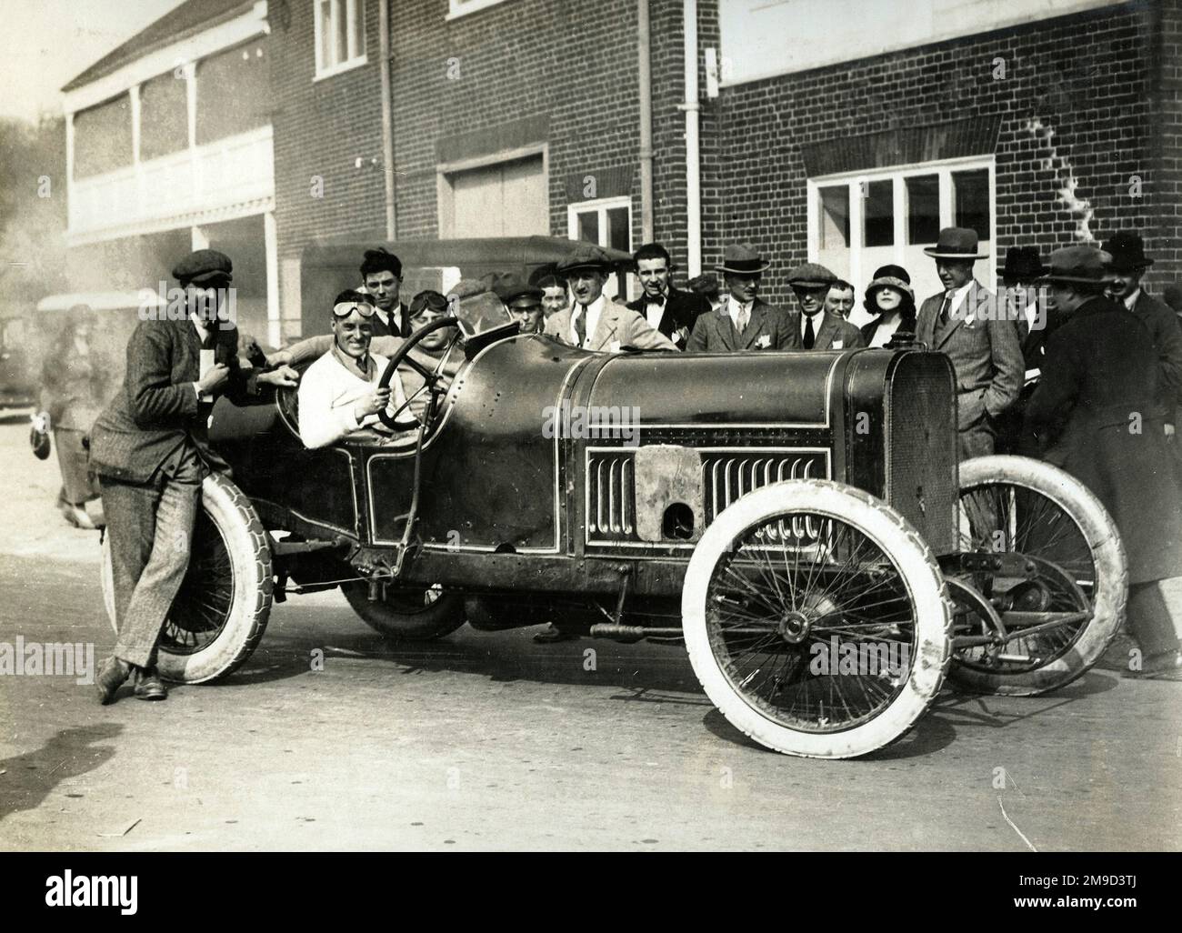 Malcolm Campbell in Peugeot im Clubhaus nach dem Gewinn von 33. 100mph Short Handicap 2. April 1923 - Brooklands - Durchschnittsgeschwindigkeit 92,25 km/h mit Beifahrer und Mann, der sich auf das Auto lehnt. Stockfoto