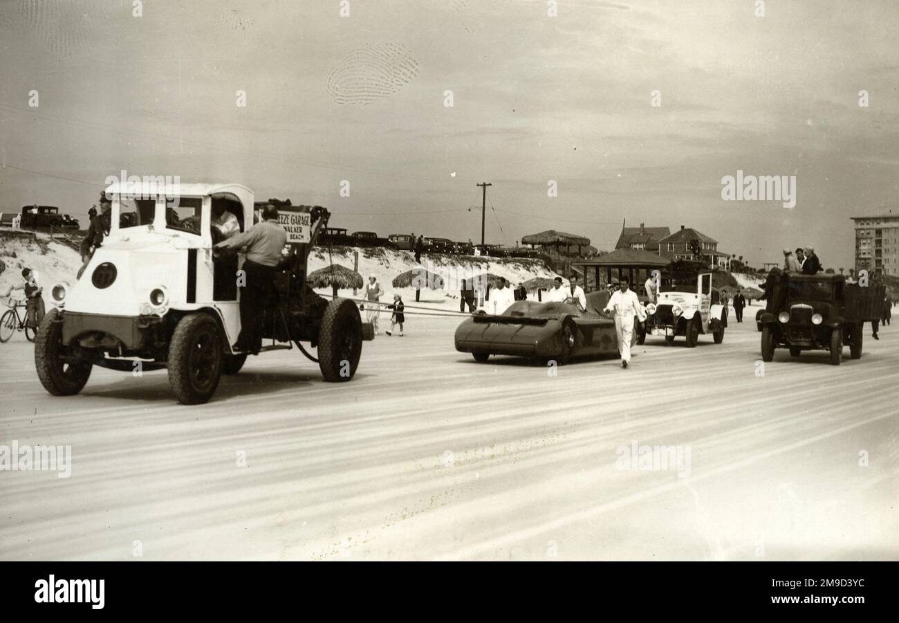 Blue Bird wird mit anderen Fahrzeugen, Mechanikern und Autos mit Dünen im Hintergrund auf Sand geschleppt. Stockfoto