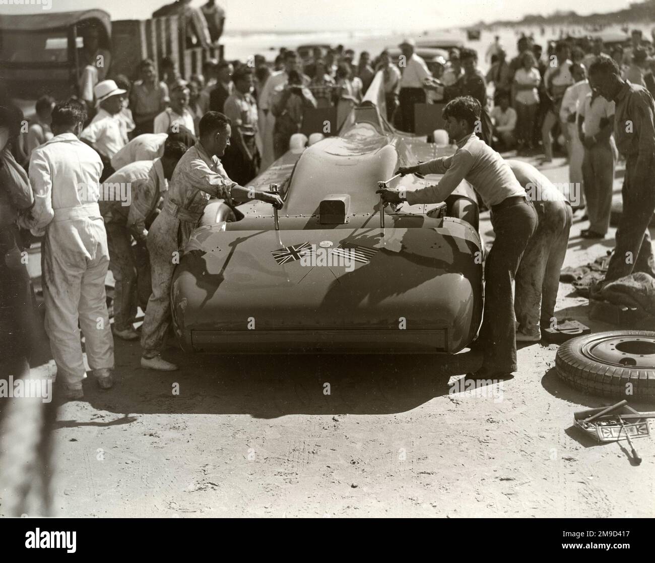 Blue Bird parkt auf Sand, wobei die Mechaniker die Abschleppstangen entfernen und Spezialreifen mit Menschenmassen anbringen. Stockfoto