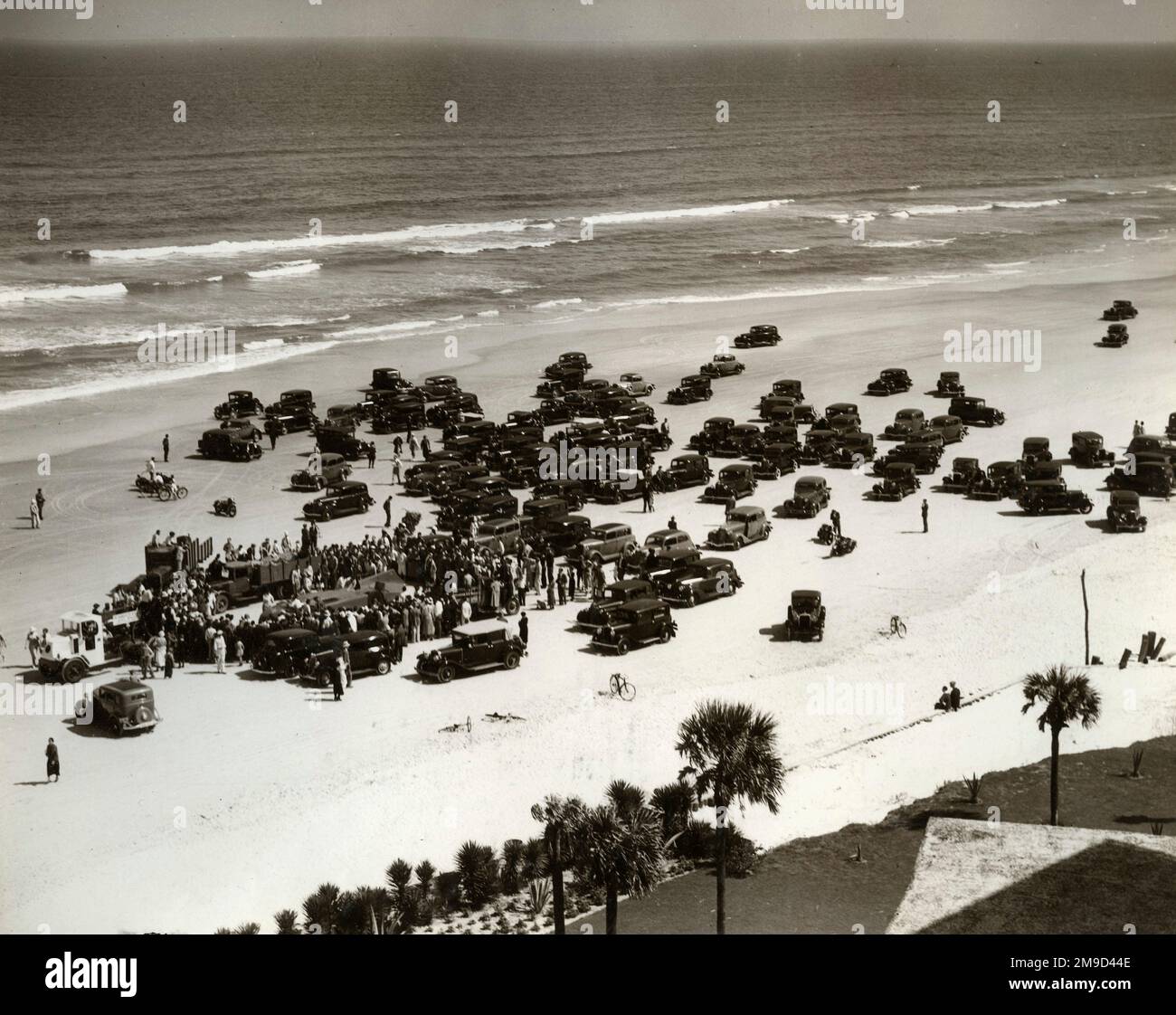 Weiter Blick auf Daytona Beach mit Blue Bird inmitten von Menschenmassen und Privatwagen mit Meer im Hintergrund. Stockfoto