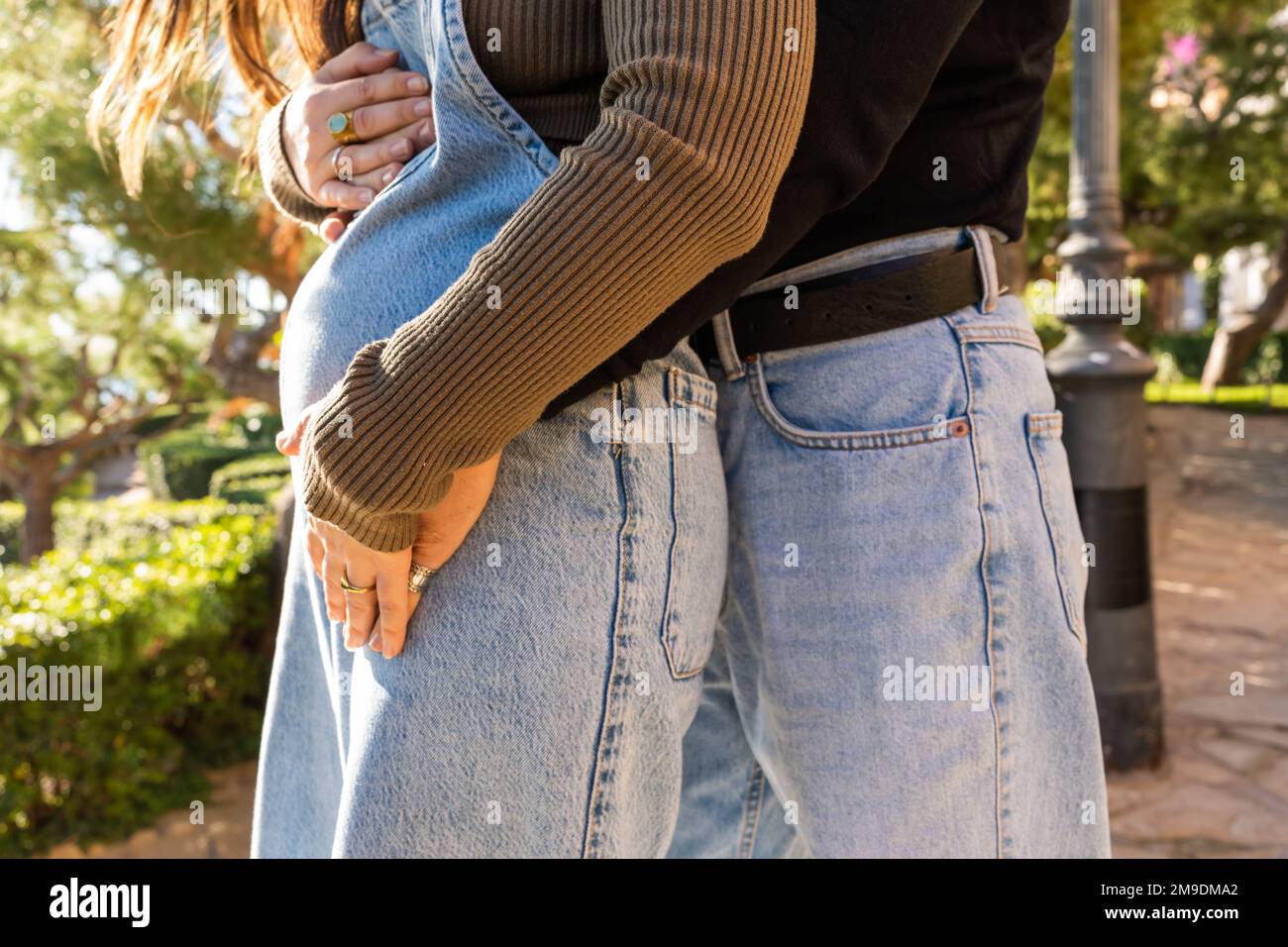 Geerntet, anonym, männlich in Jeans, berührt schwangeren Bauch von weiblich in Denim, steht auf der Straße an sonnigen Tagen Stockfoto