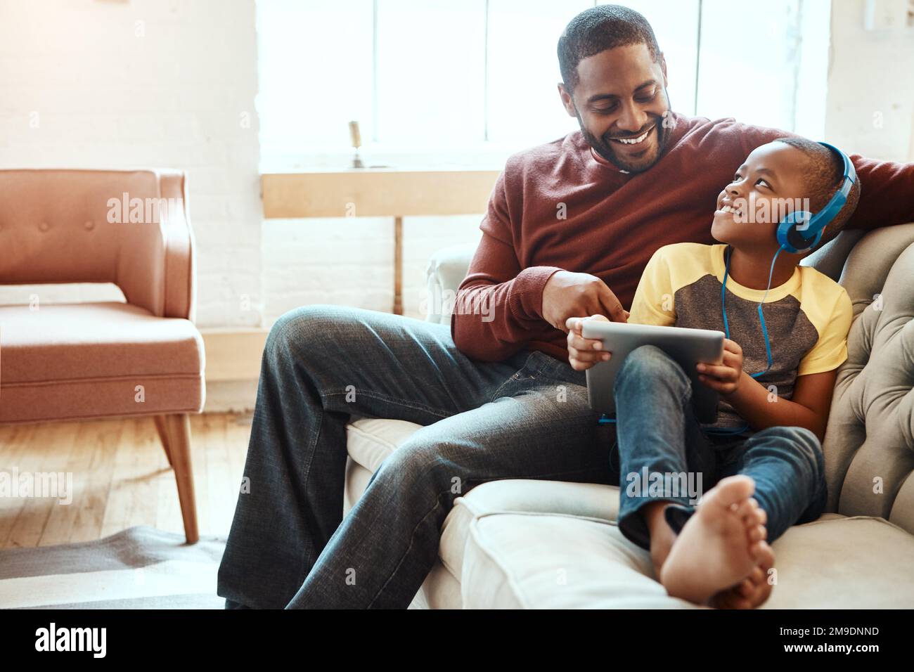 Digitales Tablet, Vater und Junge auf dem Sofa sehen sich ein lustiges, Comic- oder Meme-Video in sozialen Medien an. Fröhlicher, lächelnder und afrikanischer Mann, der einen Film mit streamt Stockfoto