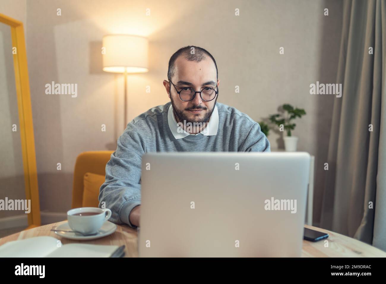 Porträt eines jungen bärtigen Mannes in trendigen Brillen, der im Home Office mit einem Laptop arbeitet. Stockfoto