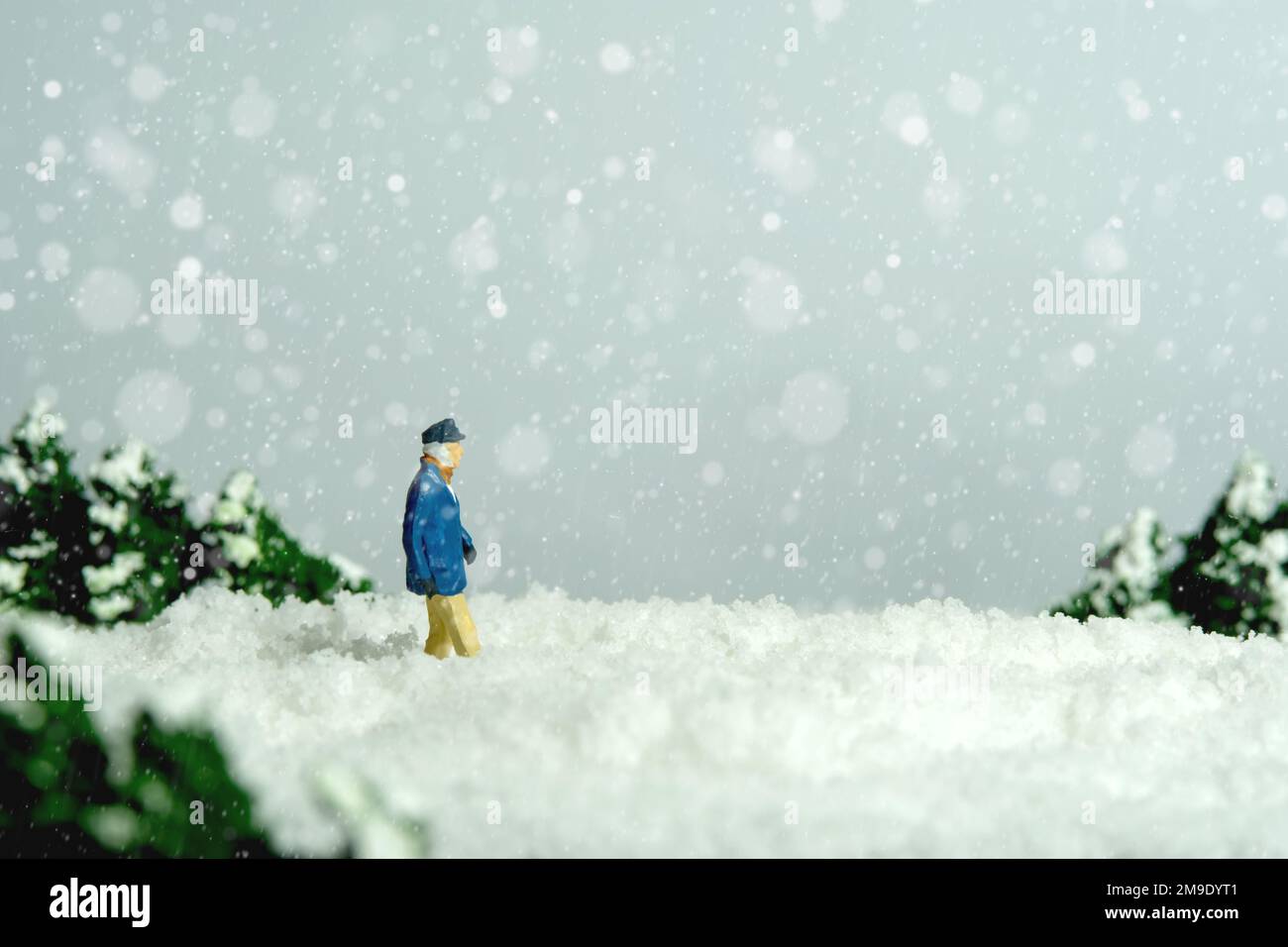 Miniatur-Menschen-Spielzeug-Figuren-Fotografie. Mobilitätsproblem im Winter. Ein alter Mann, der in einer Schneeverwehung auf der Straße läuft. Bildfoto Stockfoto