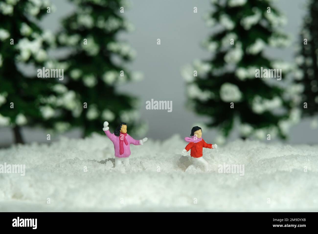 Miniatur-Menschen-Spielzeug-Figuren-Fotografie. Winterurlaub. Kinder, Bruder und Schwester, die Schneeball spielen und in den Tannenwald werfen. Bildfoto Stockfoto