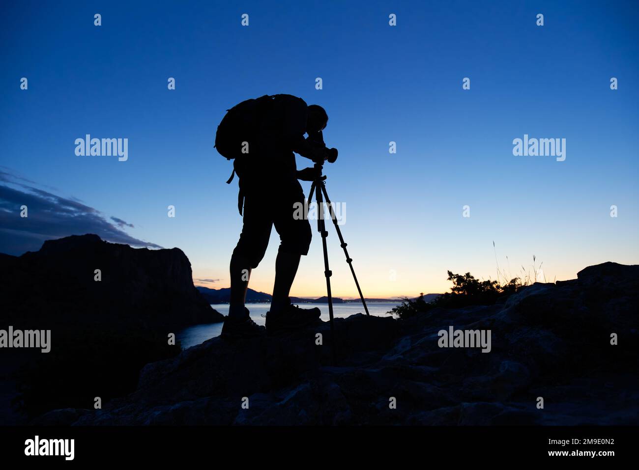 Silhouette des Fotografen auf dem Gipfel des Berges bei Sonnenuntergang. Naturfotograf in Aktion. Analoge Filmfotografie Stockfoto
