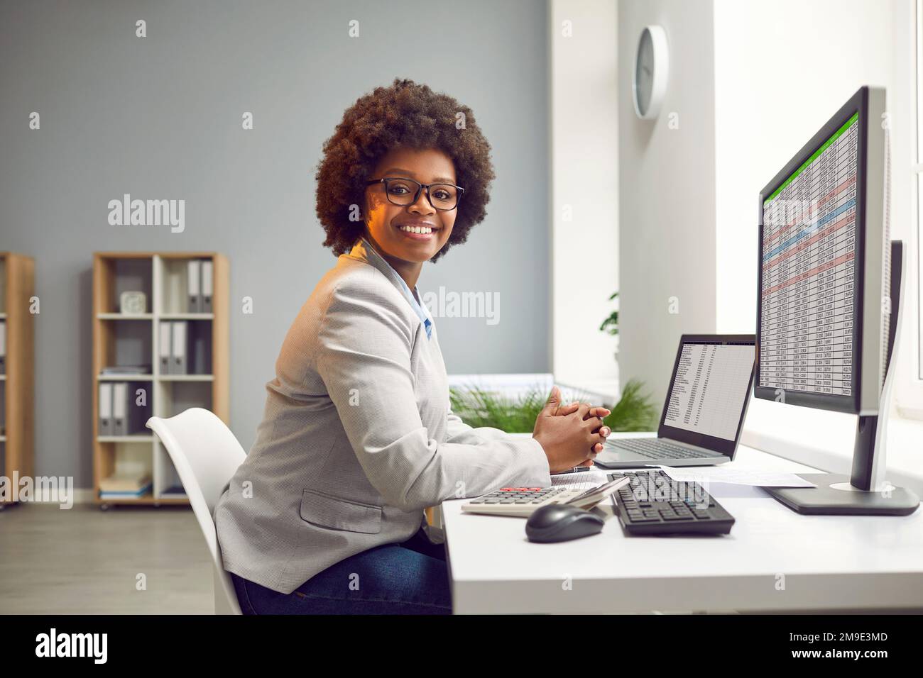Glückliche lächelnde afroamerikanische Geschäftsfrau, Buchhalterin, die an einem Laptop mit Tischen im Büro arbeitet. Stockfoto