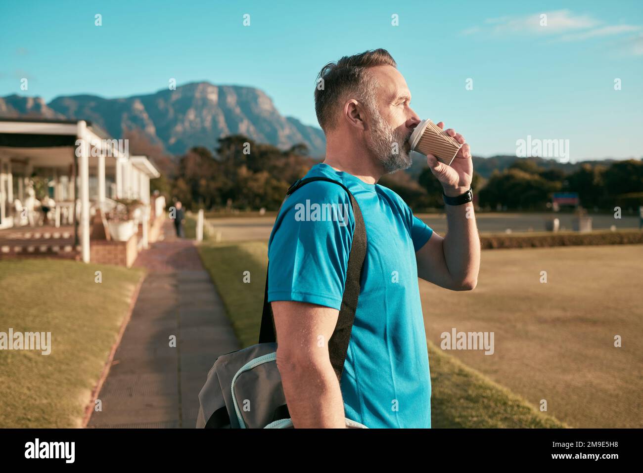 Auftanken, indem Kaffee trainiert wird. Ein hübscher, reifer Trainer steht allein draußen und genießt eine Tasse Kaffee. Stockfoto