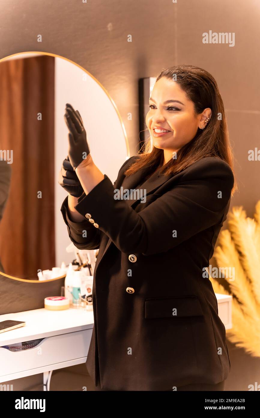 Frau lateinamerikanischer Abstammung in einem ästhetischen Augenbrauen- und Nagelladen. Porträt einer Chefin, die Handschuhe anzieht Stockfoto