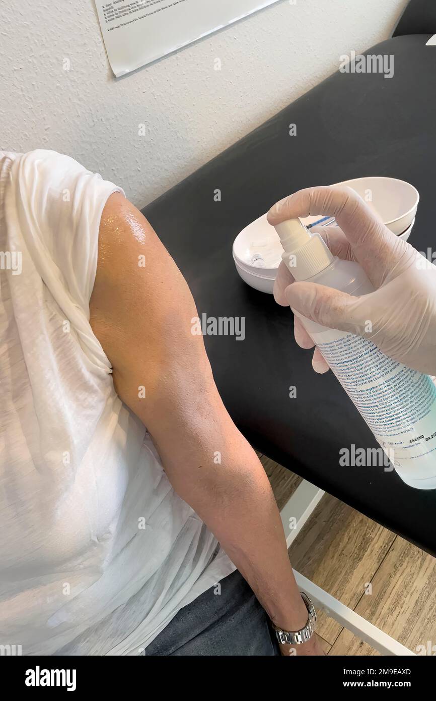 Der Arm des Patienten wird von der Arzthelferin mit medizinischem Desinfektionsspray Oberer Arm vor der Injektion für Impfung Booster gegen desinfiziert Stockfoto