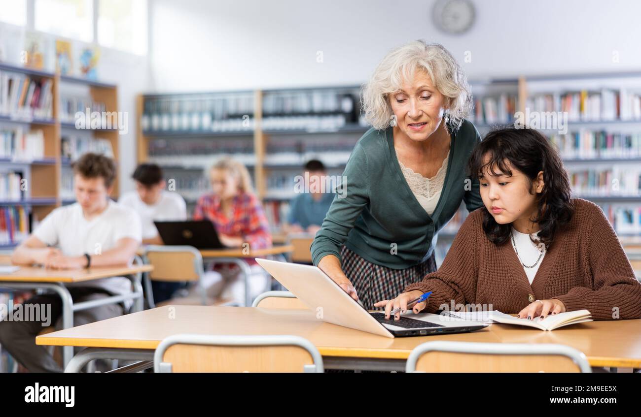 Ältere Lehrerin hilft Schülerinnen, die Gleichung in der Schulbibliothek zu lösen Stockfoto