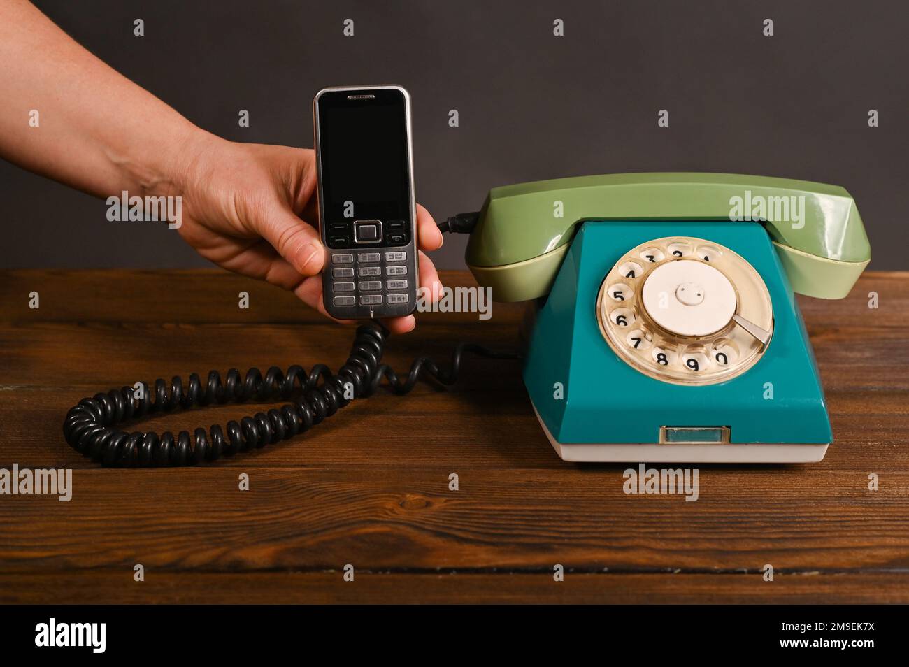 Ein altes Handy mit Knopfdruck in der Hand einer Frau neben einem alten Wähltelefon. Stockfoto