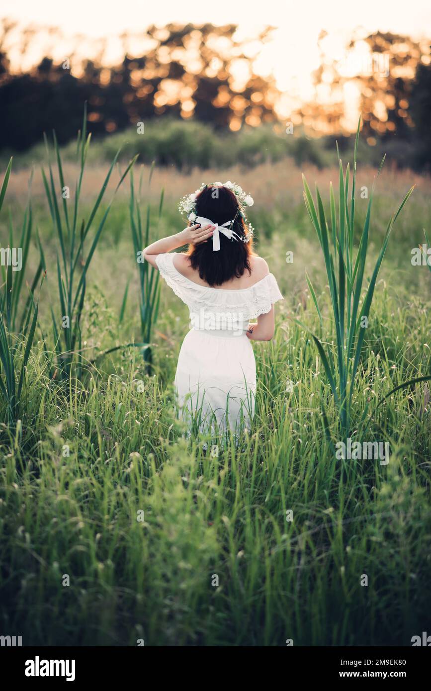Ein Mädchen in einem weißen Kleid mit Blumenkranz steht im Sommer auf dem Feld. Das Konzept von Einheit, Liebe und Fürsorge für die Natur Stockfoto