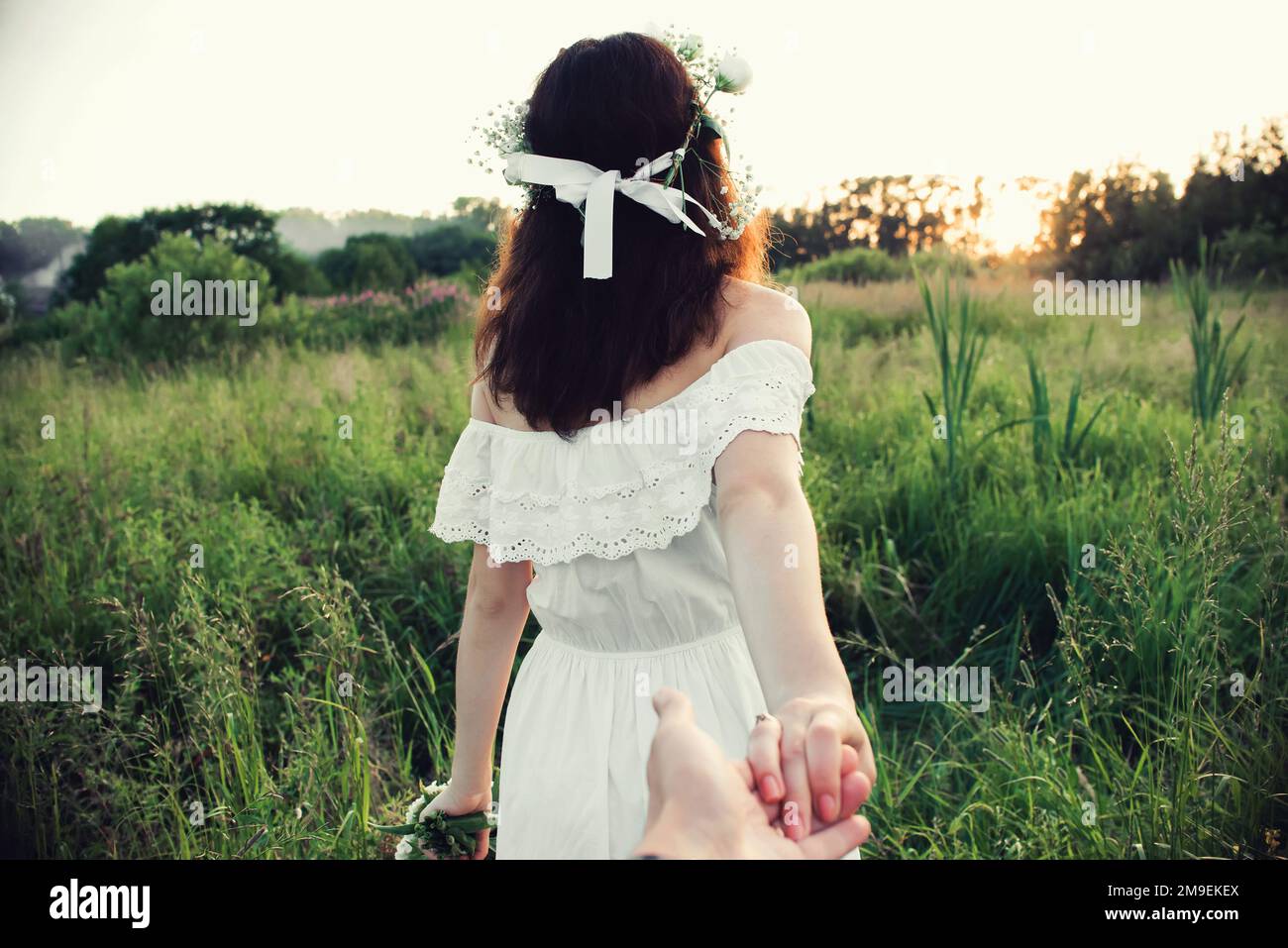 Folgen Sie mir. Der Rücken eines Mädchens, das die Hand ihres Freundes auf einem Feld in der Natur hält Stockfoto