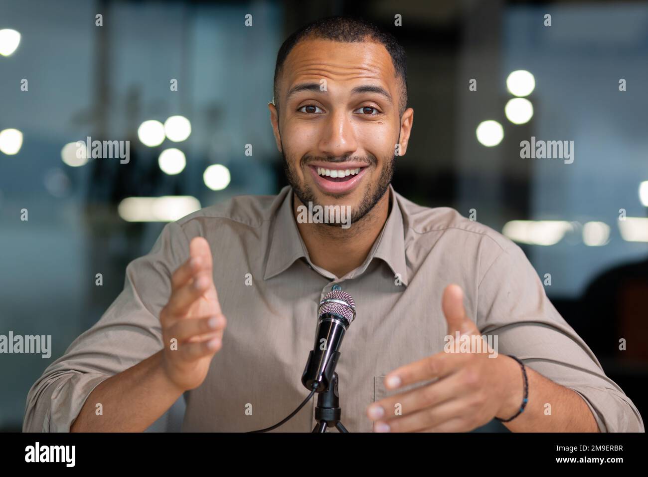 Erfolgreicher hispanischer Mann im Büro, der in die Kamera schaut und auf Video spricht, zwei im Büro, Geschäftsmann, der Audio-Podcast mit professionellem Mikrofon aufnimmt, Webcam-View-pov. Stockfoto