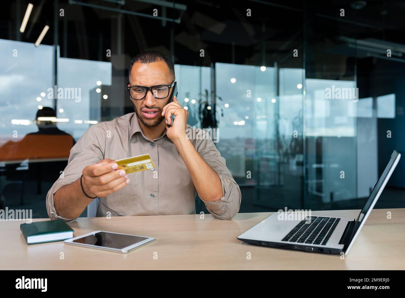 Ein unzufriedener Geschäftsmann im Büro mit einer Bankkreditkarte ruft den Kundendienst an, ein Mann mit gesperrter Karte kann keinen Kauf in einem Online-Shop tätigen. Stockfoto