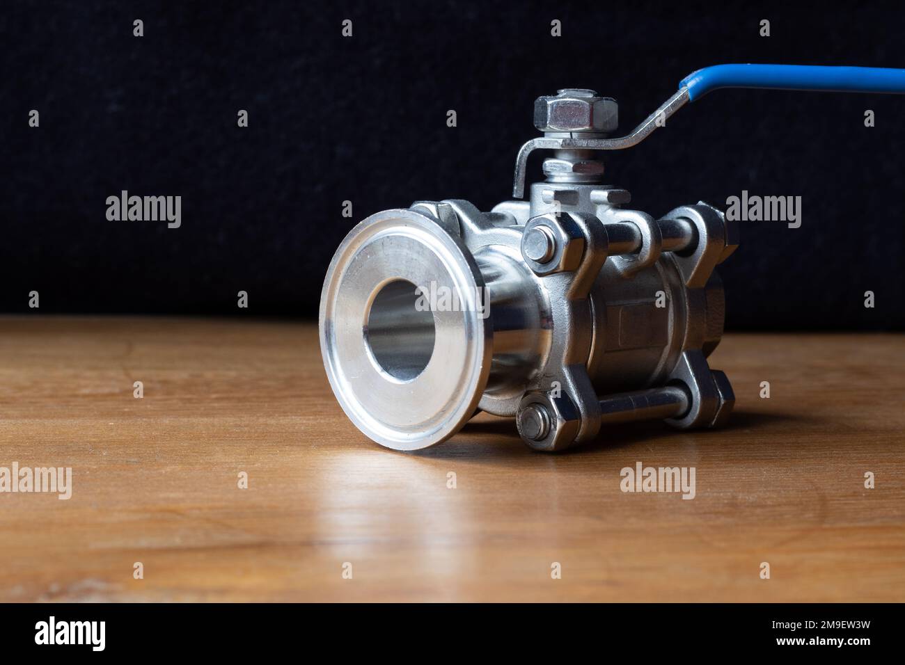 Dreiteiliges Kugelventil, eine Durchflussregeleinrichtung, die den Flüssigkeitsfluss steuert. Kopieren Sie auf einem Holztisch den Platz nach links. Stockfoto