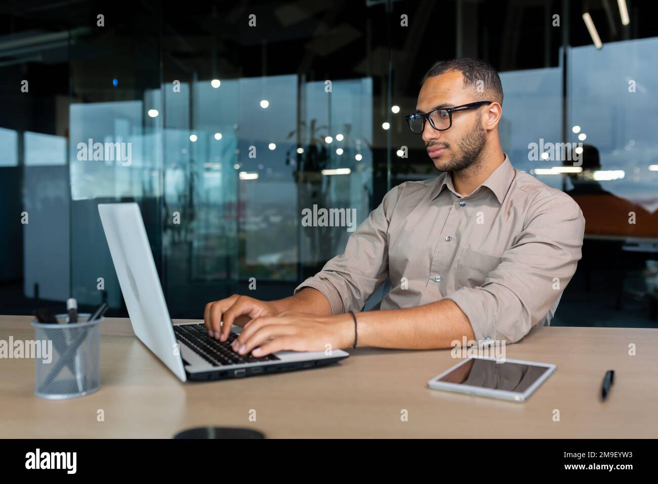 Seriöser und konzentrierter hispanischer Programmierer, der im Büro arbeitet, Mann im Hemd, der Codes für Software mit einem Laptop schreibt. Stockfoto