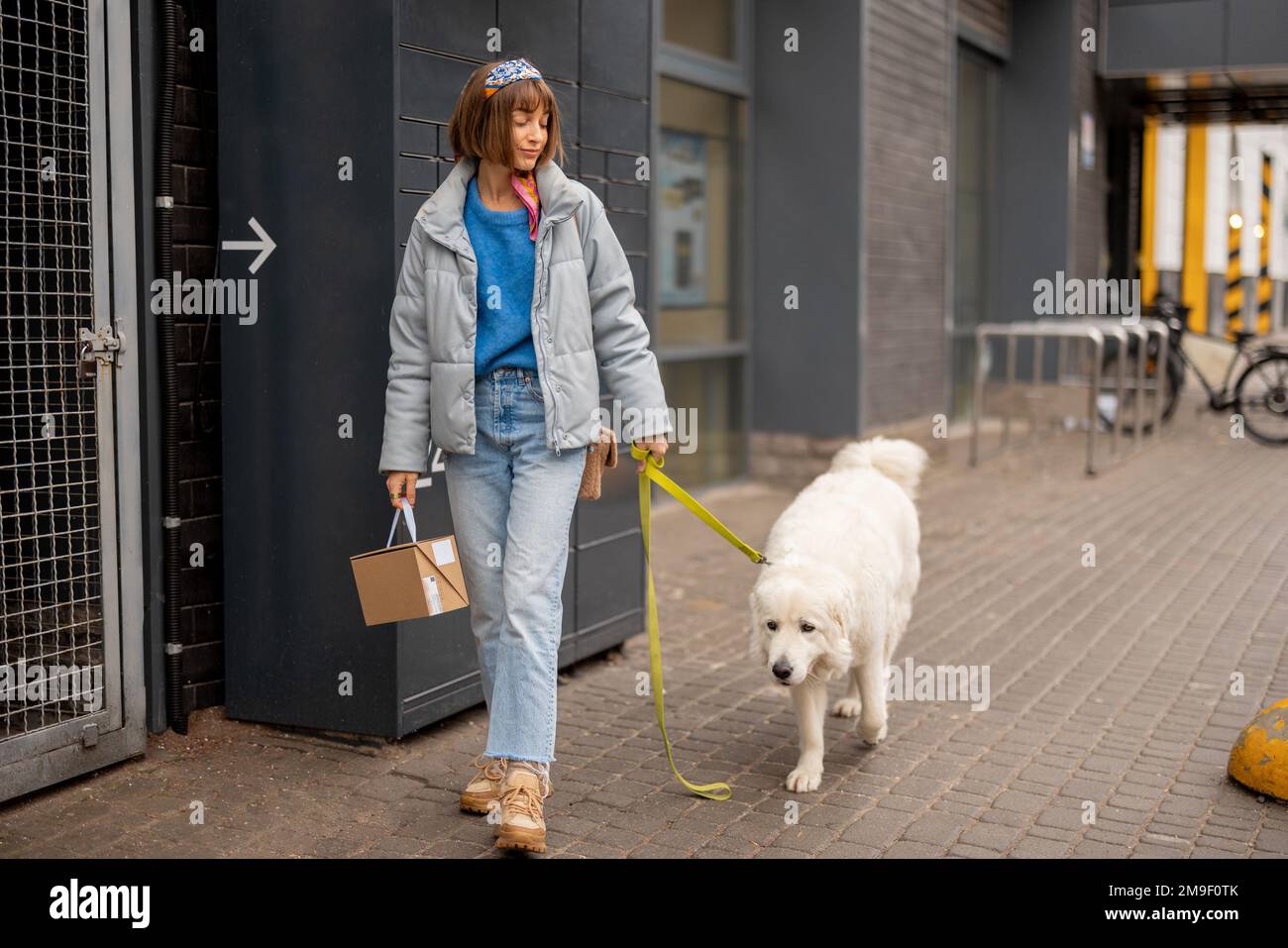Eine Frau geht mit einem Hund und einem Paket auf einer Straße Stockfoto