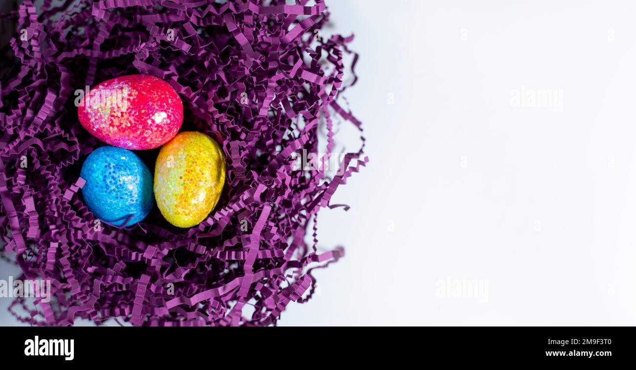 Frohe Osterkarte. Ostereier auf dem Hintergrund eines violetten Nests, Draufsicht auf weißem Hintergrund, Bild mit selektivem Fokus. Platz für Text kopieren. Stockfoto