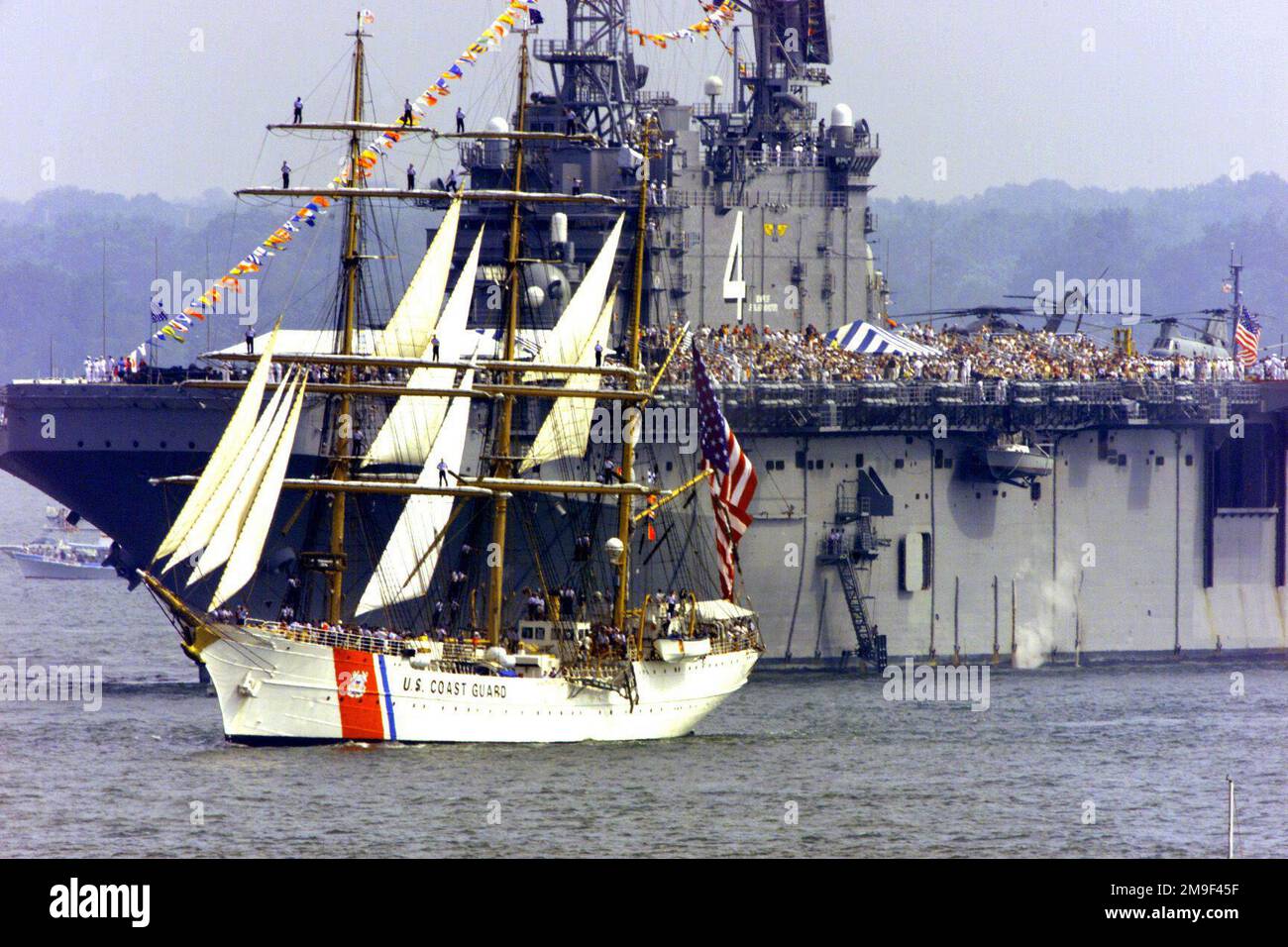 Das Flaggschiff Eagle der US Coast Guard Academy segelt an der USS Nassau (LHA 4) entlang und in Hampton Roads, Virginia, am Eröffnungstag von OpSail 2000. Hampton Roads ist Gastgeber von OpSail am 2000 16-18. Juni und wird Dutzende von Großschiffen aus der ganzen Welt präsentieren. Basis: USS Harry S. Truman (CVN 75) Staat: Virginia (VA) Land: Vereinigte Staaten von Amerika (USA) Stockfoto