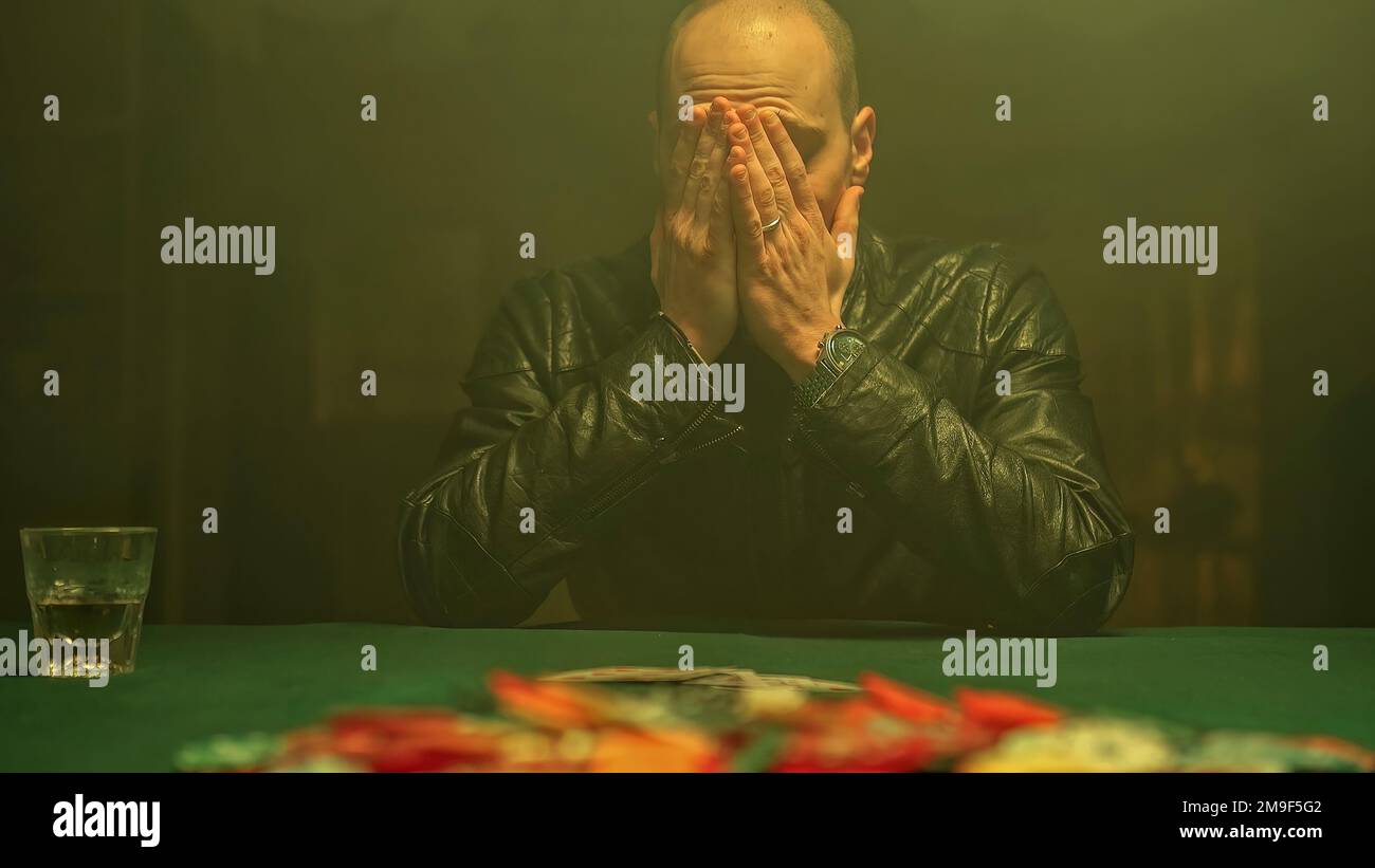 Ein aufgeregter Pokerspieler gewinnt das Spiel, zeigt seine Karten, während er Whiskey trinkt, und nimmt alle auf dem Tisch verteilten Pokerchips. Gewinnen im Gambli Stockfoto