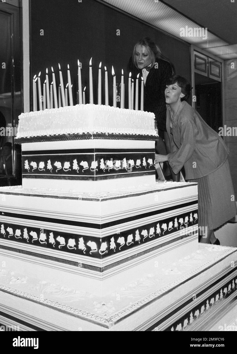 Ein gigantischer 6ft-Hochzeitstorte zum 29. Geburtstag des längsten Stücks der Welt, der verstorbenen Dame Agatha Christies Mausefalle, die im Savoy Hotel in London von der scheidenden Hauptdarstellerin Helen Lloyd (r), Und die neue Hauptdarstellerin, Mary Tempest, in der Rolle, die ursprünglich von Sheila SIM (Lady Attenborough) geschaffen wurde. Helen und Mary werden gesehen, wie sie eine Trittleiter hochklettern, um die Kerzen auszublasen. Stockfoto