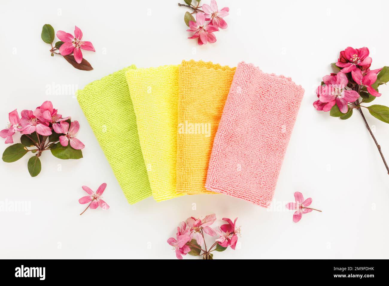 Neues gefaltetes Mikrofasertuch zur Reinigung auf weißem Hintergrund mit Frühlingsblumen. Reinigungstücher aus Mikrogewebe zum Staubwischen und Polieren. Haushaltsreinigungsdienstkonzept. Draufsicht Stockfoto
