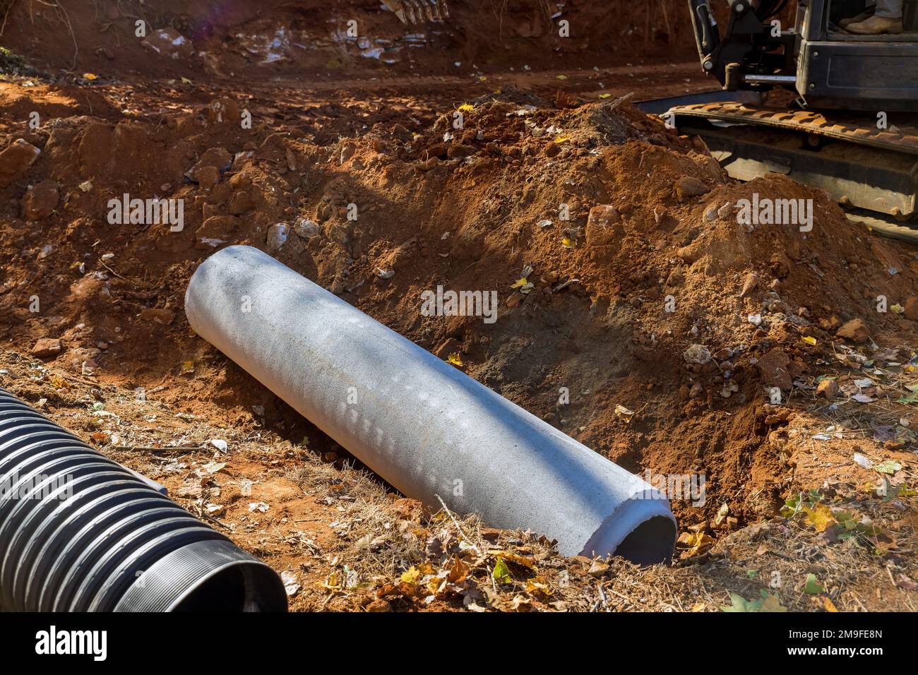 Arbeiter, der Abwasserrohre in den Boden legt, bereitet vor, Betonrohre unterirdisch zu verlegen Stockfoto