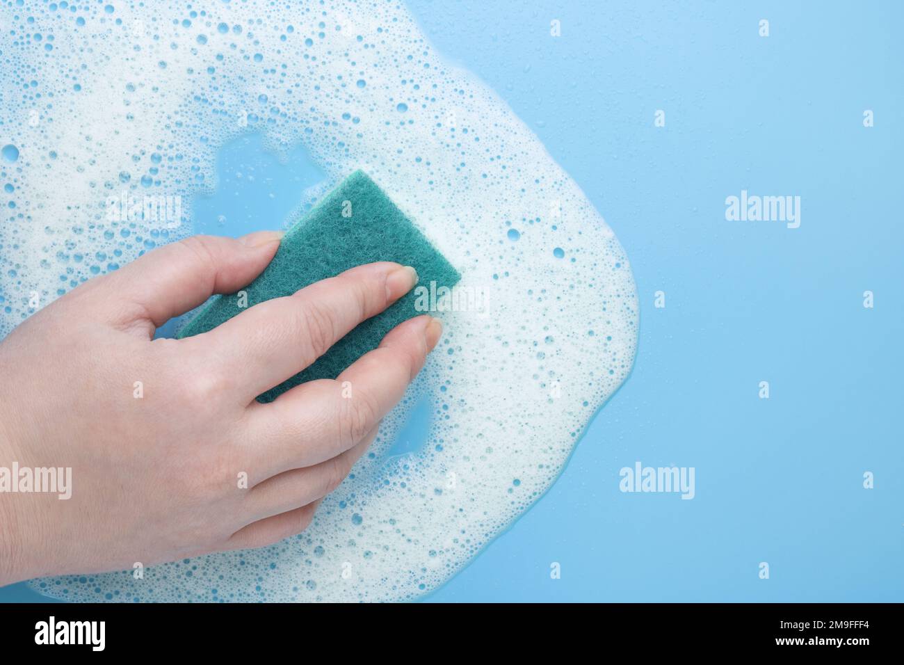 Weibliche Hand mit einem Reinigungsschwamm aus weißem Schaum, Mousse auf blauem Hintergrund. Das Konzept der Schaumprodukte, Reinigungsmittel oder Reinigungsmittel. Stockfoto