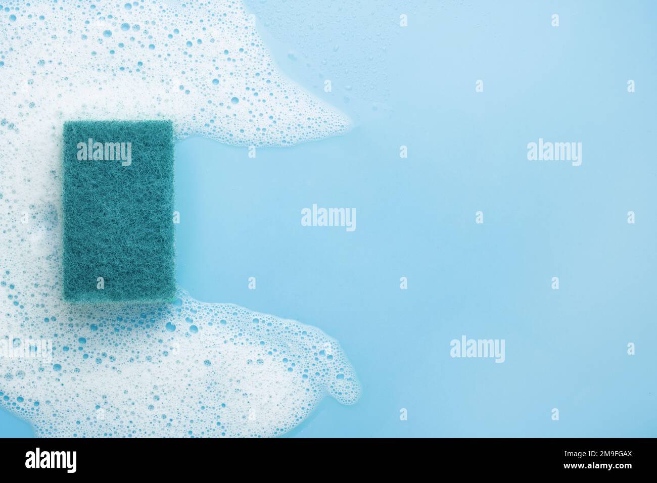 Ein Reinigungsschwamm aus weißem Schaum, Mousse, auf blauem Hintergrund. Rahmen für Text. Das Konzept der Schaum-, Reinigungs- oder Reinigungsmittel. Stockfoto