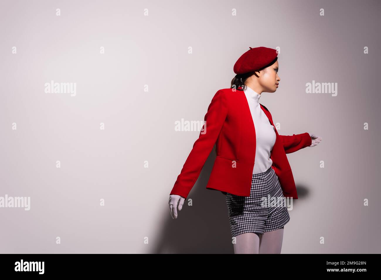 Seitenansicht der modischen asiatischen Frau in Baskenmütze und Shorts auf grauem Hintergrund mit Schatten Stockfoto