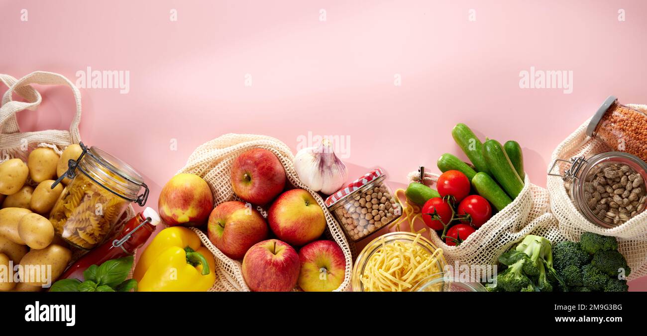 Draufsicht auf appetitliche frische rohe Äpfel Kartoffeln Kirschtomaten Gurken Brokkoli und gelber Paprika in umweltfreundlichen Baumwollsäcken auf Pink Stockfoto