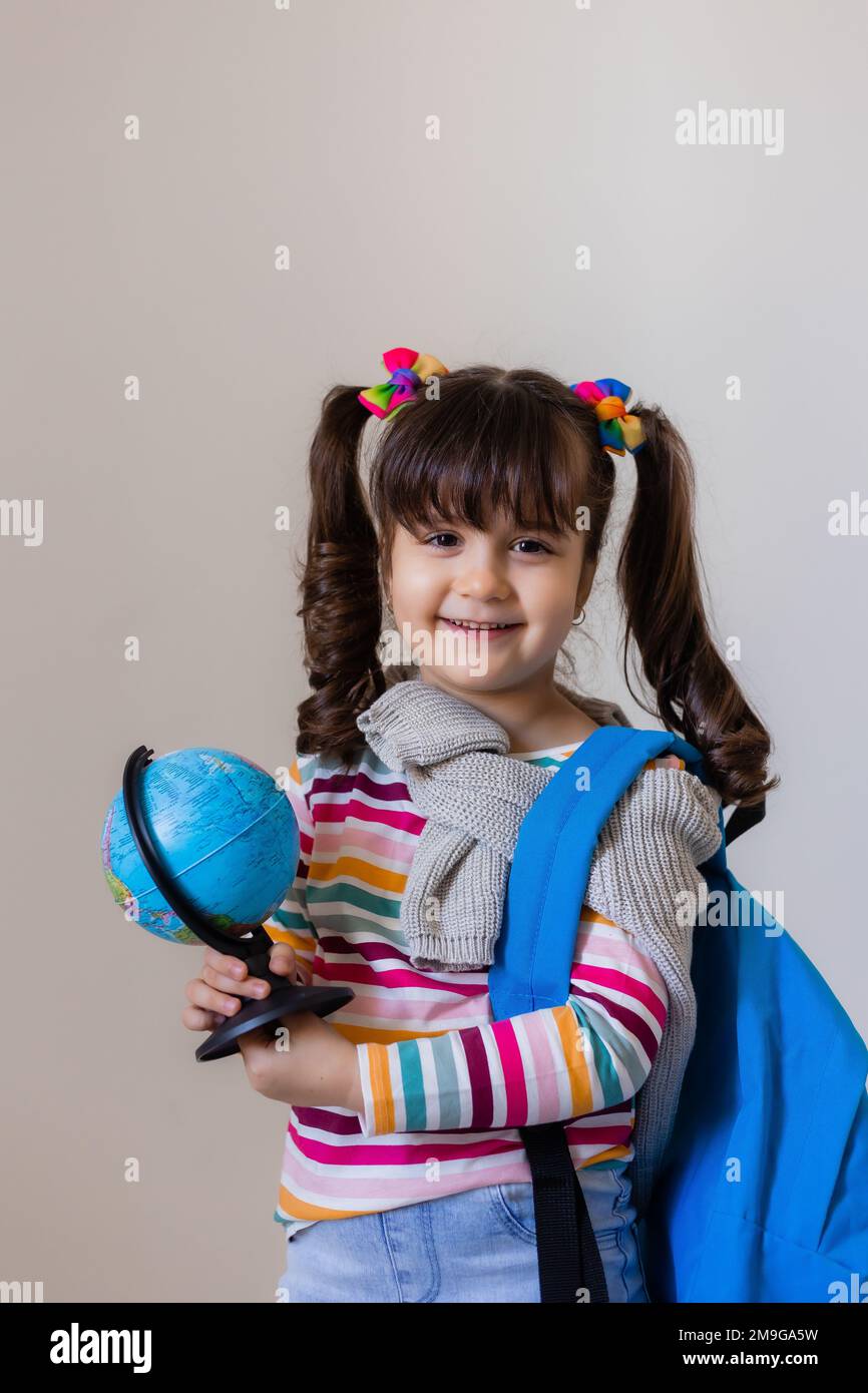 Ein glückliches kleines Vorschulmädchen mit einem Rucksack und einem Globus auf hellem Hintergrund, Platz für Text. Vorschulerziehung, Reisen mit Kindern Stockfoto