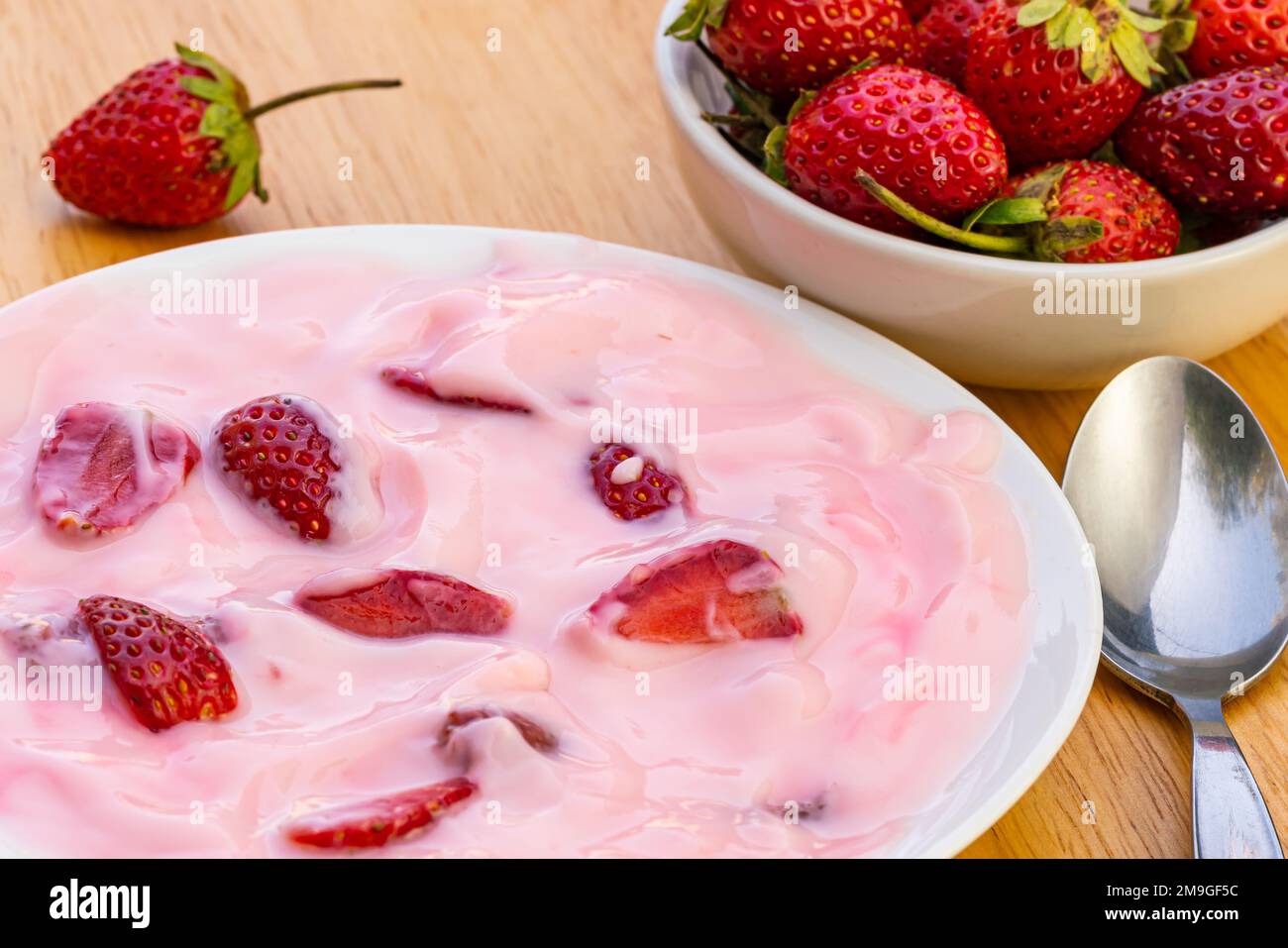 Blick aus einem hohen Winkel auf köstlichen Erdbeerjoghurt mit Erdbeerstücken in weißer Keramikschale und frisch reife Erdbeerfrüchte in Keramikschale auf Woo Stockfoto
