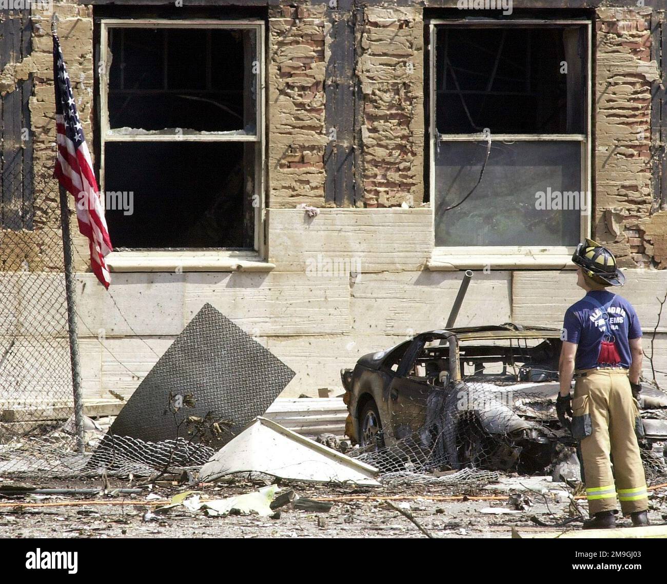 Vor einem ausgebrannten Wagen inspiziert ein Feuerwehrmann von Alexandria den Schaden am Pentagon. Die US-Flagge wird außerhalb des Pentagon gesetzt, nachdem ein entführter American Airlines Flug 77, eine Boeing 757-200 absichtlich ins Pentagon gestürzt wurde, am 11. September 2001. Der Anschlag des Pentagon folgte einem Angriff auf die Zwillingstürme des New York World Trade Center, wo zwei voll beladene Passagierflugzeuge in die Gebäude geflogen wurden, was als der schlimmste Terroranschlag der Geschichte bezeichnet wird. Basis: Pentagon Staat: District of Columbia (DC) Land: United States of America (USA) Scene Major Co Stockfoto