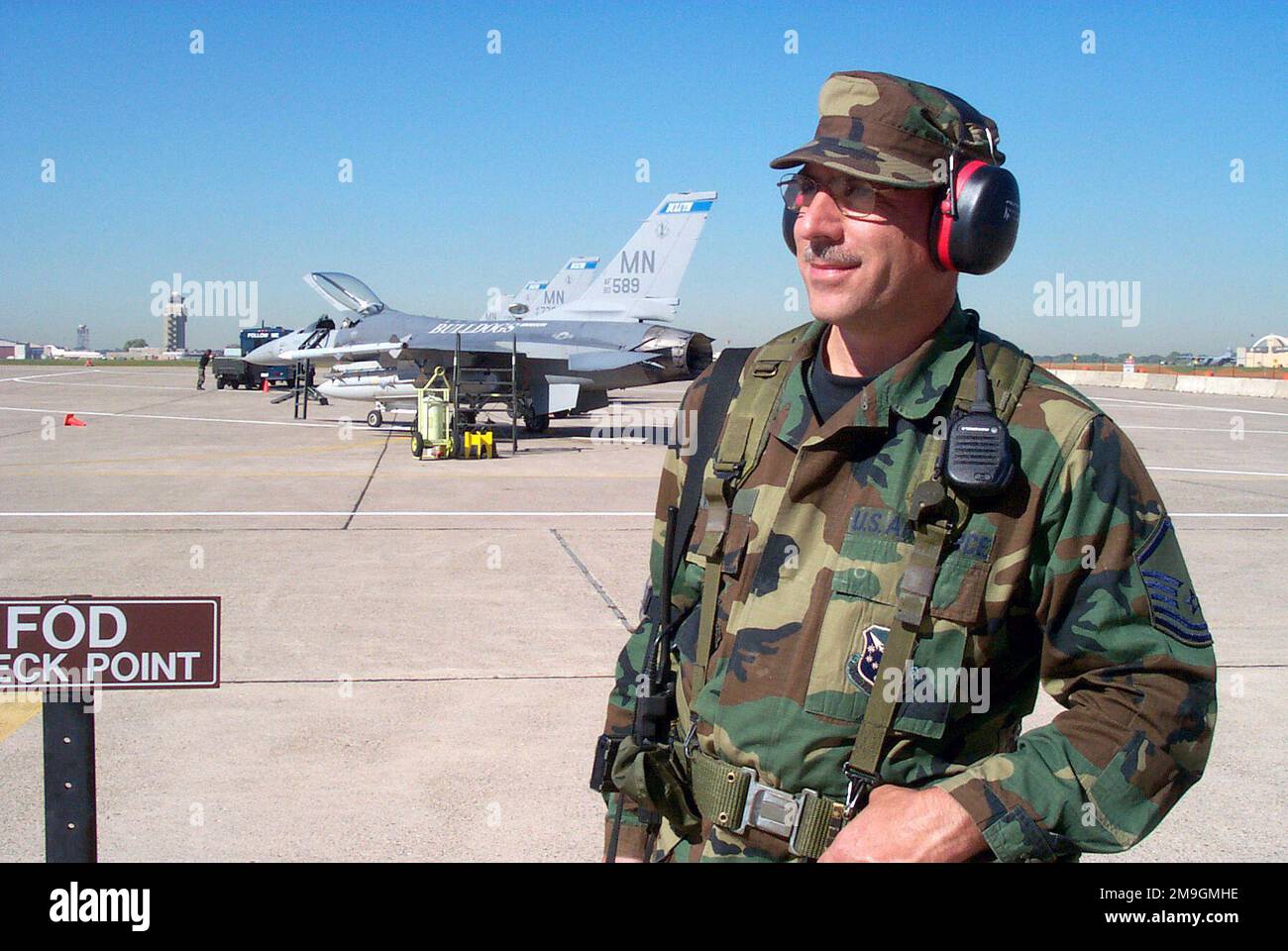 Während F-16 im Hintergrund gegen Falcons aus dem 148. Kampfflug kämpft, steht MASTER Sergeant (MSGT) Daniel Toay, USAF, 148. Wartungsgeschwader, Minnesota Air National Guard, wachsam außerhalb eines der eingeschränkten Wing-Gebiete am 27. September 2001. MSGT Toay meldete sich freiwillig für zusätzliche Aufgaben als Sicherheitserweiterungsbeauftragter zusätzlich zu seinen normalen Wartungsaufgaben. MSGT Toay ist eines von etwa 25 Mitgliedern der Einheit, die die bestehenden Sicherheitskräfte im 148. Kampfflugflügel zur Unterstützung der Operation ADLER verstärkt. Subjekt Operation/Serie: ADLERBASIS Duluth Praktikant Stockfoto